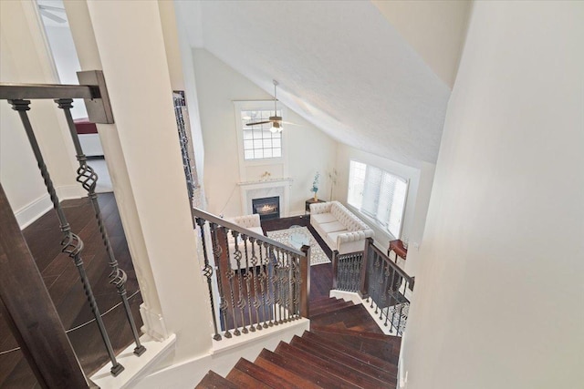 stairs featuring hardwood / wood-style flooring, vaulted ceiling, ceiling fan, and a fireplace