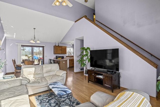 living room featuring lofted ceiling, a healthy amount of sunlight, a notable chandelier, and light hardwood / wood-style floors