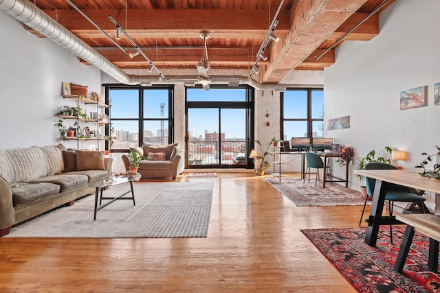 living room featuring wood ceiling, rail lighting, a high ceiling, wood-type flooring, and brick wall