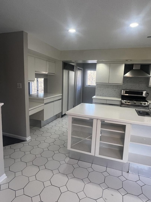 kitchen featuring gas range, wall chimney range hood, white cabinets, and backsplash