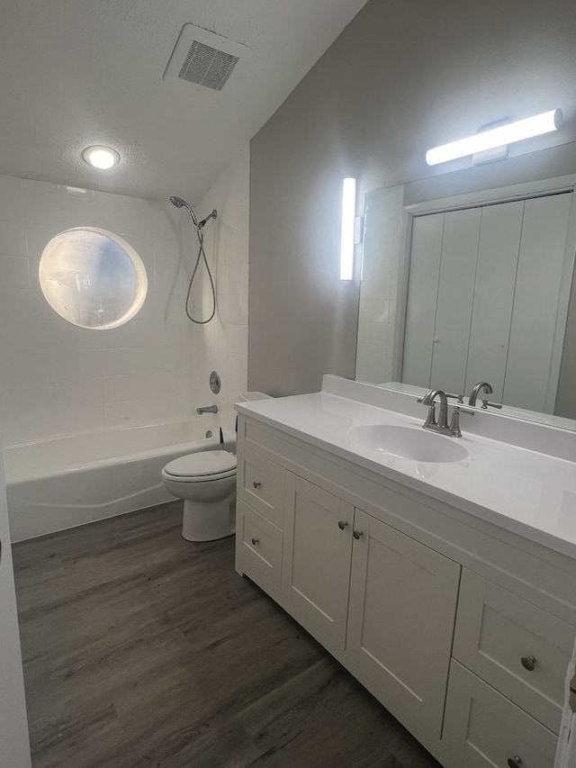 full bathroom featuring wood-type flooring, vanity,  shower combination, toilet, and a textured ceiling