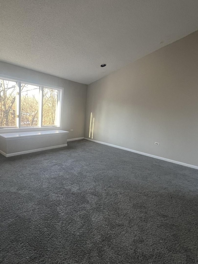 empty room with dark colored carpet and a textured ceiling