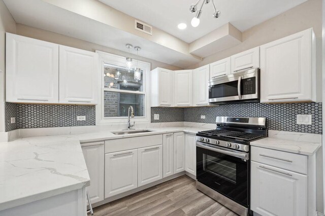 kitchen with pendant lighting, white cabinets, stainless steel appliances, sink, and light stone counters