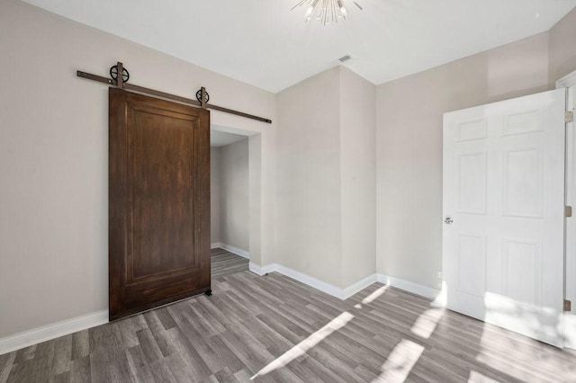 unfurnished bedroom with a notable chandelier, a barn door, and light hardwood / wood-style floors