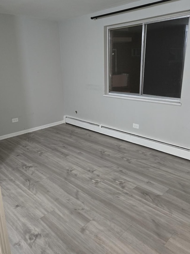 unfurnished room featuring a baseboard heating unit and light hardwood / wood-style floors