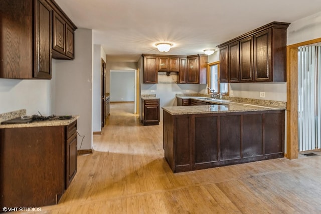 kitchen featuring light wood-type flooring, dark brown cabinetry, sink, kitchen peninsula, and light stone counters