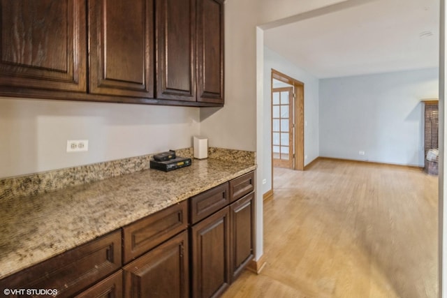 kitchen with light stone counters, dark brown cabinetry, and light wood-type flooring