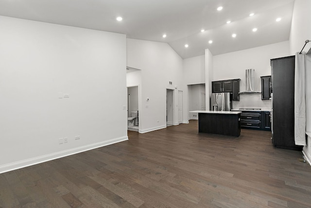 kitchen with stainless steel appliances, wall chimney range hood, dark hardwood / wood-style flooring, backsplash, and an island with sink