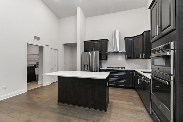 kitchen with a high ceiling, a center island, dark hardwood / wood-style floors, wall chimney range hood, and stainless steel appliances