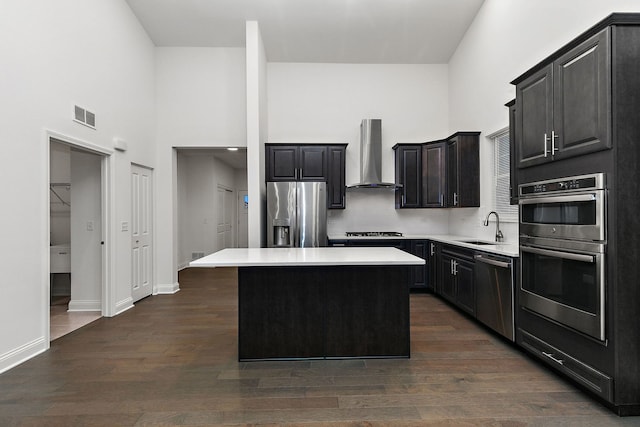 kitchen featuring appliances with stainless steel finishes, a center island, wall chimney exhaust hood, dark wood-type flooring, and sink