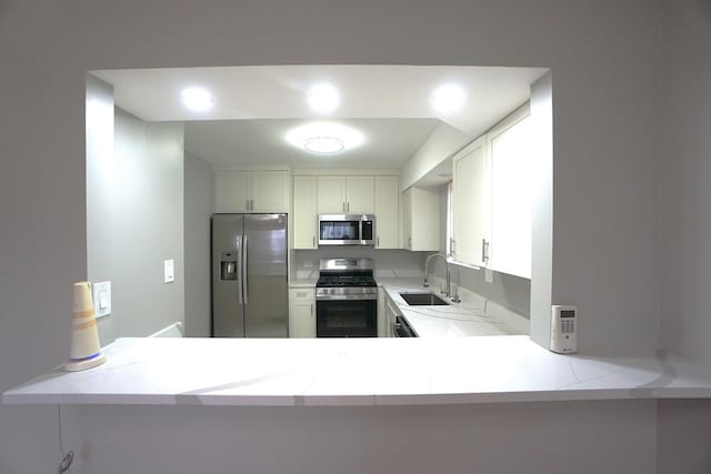 kitchen with kitchen peninsula, appliances with stainless steel finishes, sink, white cabinetry, and light stone countertops