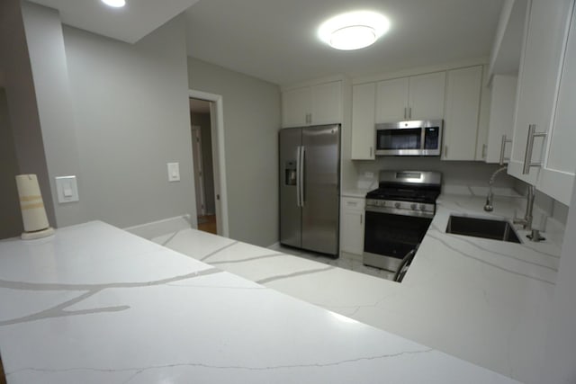 kitchen with light stone countertops, appliances with stainless steel finishes, white cabinetry, sink, and kitchen peninsula