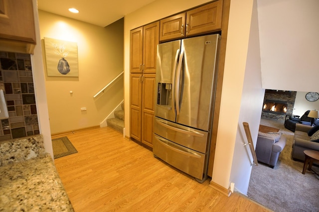 kitchen featuring light stone counters, a fireplace, stainless steel fridge, and light hardwood / wood-style flooring