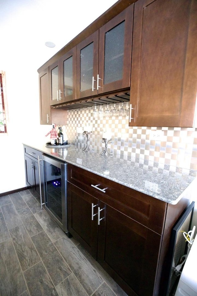 bar featuring light stone countertops, dark brown cabinets, wine cooler, and backsplash