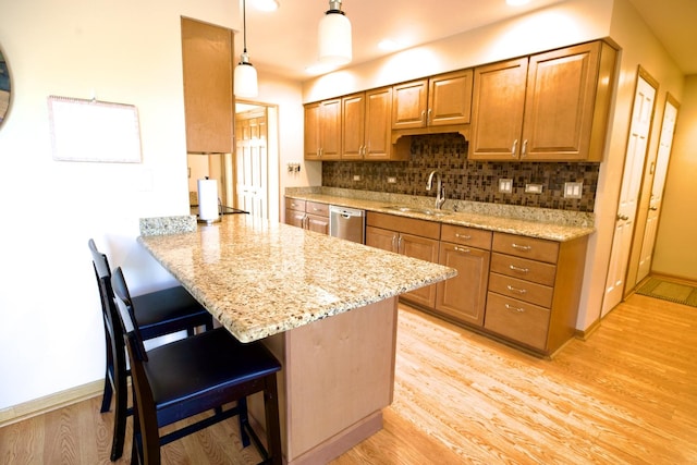 kitchen featuring a kitchen bar, sink, hanging light fixtures, stainless steel dishwasher, and kitchen peninsula