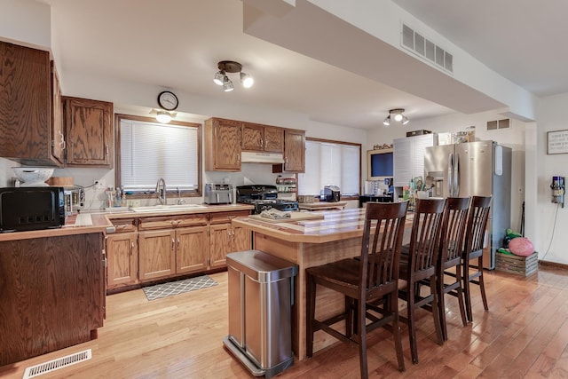 kitchen featuring stove, a kitchen breakfast bar, sink, light wood-type flooring, and stainless steel fridge