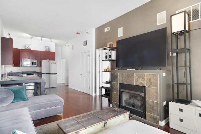 living room with rail lighting, a tile fireplace, and dark wood-type flooring