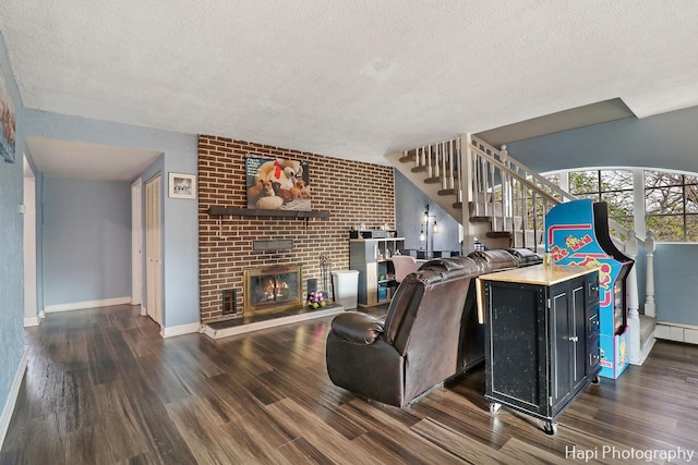 living room featuring dark wood-type flooring, a textured ceiling, a baseboard heating unit, and a brick fireplace