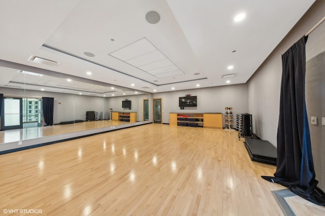 workout room with light wood-type flooring, a raised ceiling, visible vents, and recessed lighting