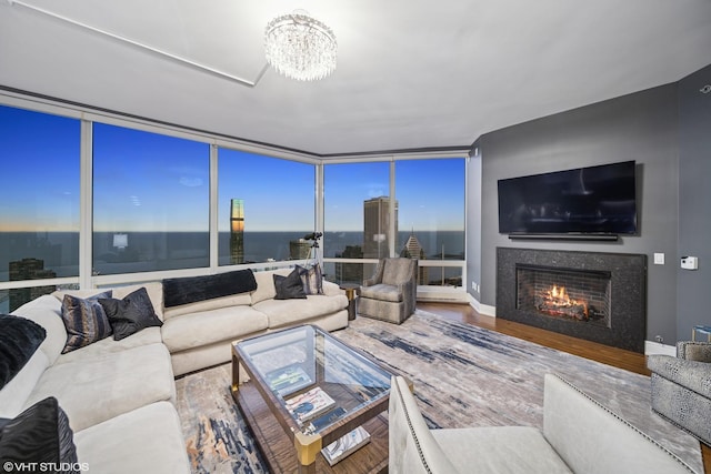 living area featuring baseboards, a chandelier, wood finished floors, a lit fireplace, and floor to ceiling windows