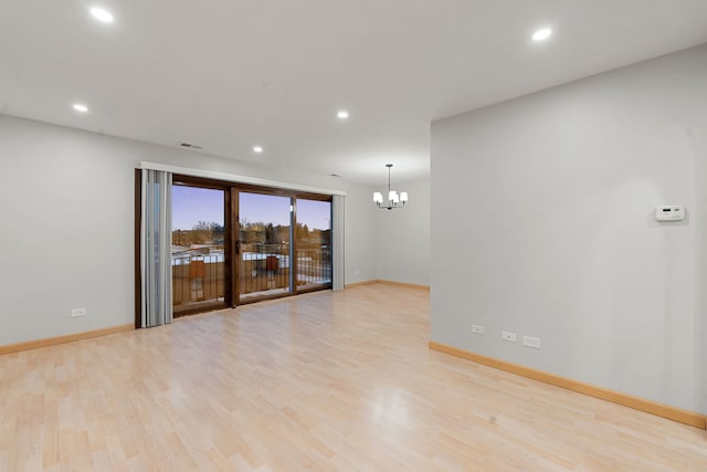 unfurnished room featuring a notable chandelier and light wood-type flooring