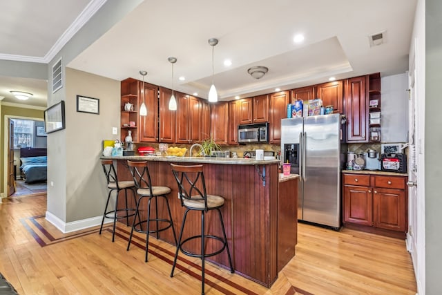 kitchen featuring appliances with stainless steel finishes, pendant lighting, a kitchen breakfast bar, kitchen peninsula, and a raised ceiling