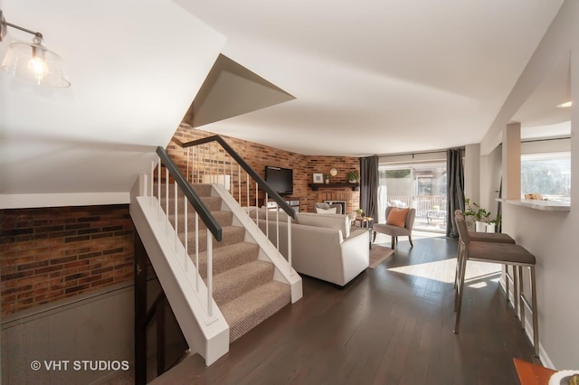 living room with brick wall, plenty of natural light, and dark wood-type flooring