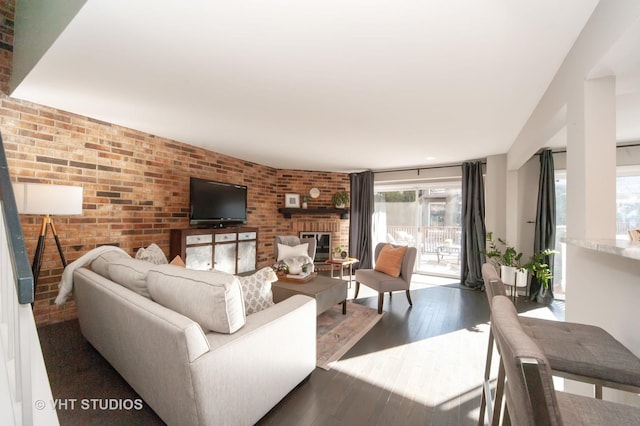 living room with a brick fireplace, dark wood-type flooring, and brick wall