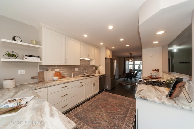 kitchen featuring dishwashing machine, sink, stainless steel fridge, white cabinetry, and light stone counters