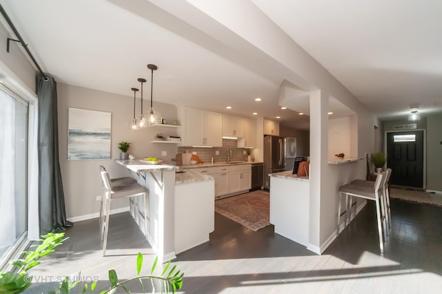 kitchen featuring a breakfast bar, hanging light fixtures, tasteful backsplash, light stone countertops, and white cabinets