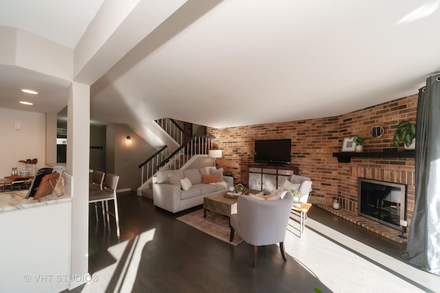 living room featuring a brick fireplace, dark wood-type flooring, and brick wall