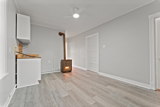 unfurnished living room with light hardwood / wood-style floors, a wood stove, and ceiling fan