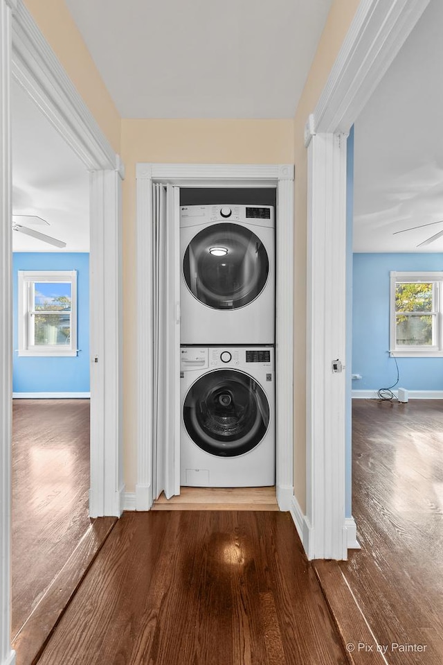 laundry area featuring ceiling fan, plenty of natural light, hardwood / wood-style flooring, and stacked washer and dryer