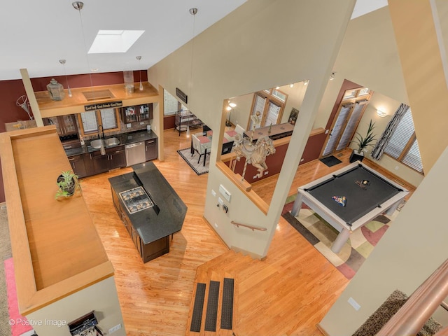 living room featuring a towering ceiling, sink, light wood-type flooring, and a skylight