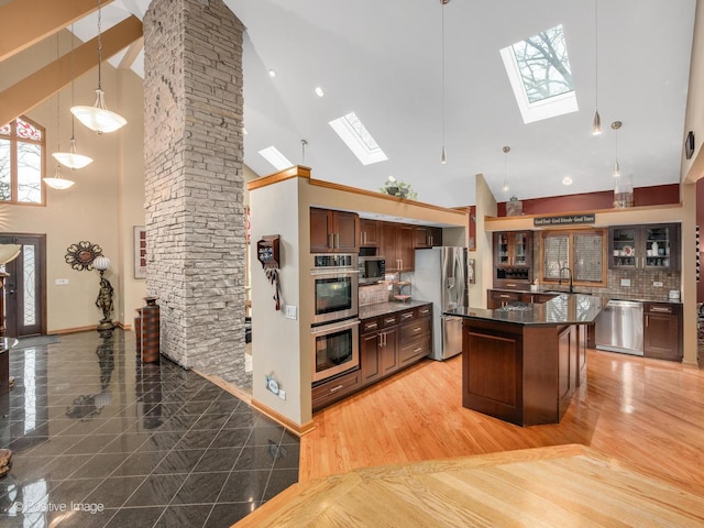 kitchen with high vaulted ceiling, stainless steel appliances, a center island, decorative backsplash, and decorative light fixtures