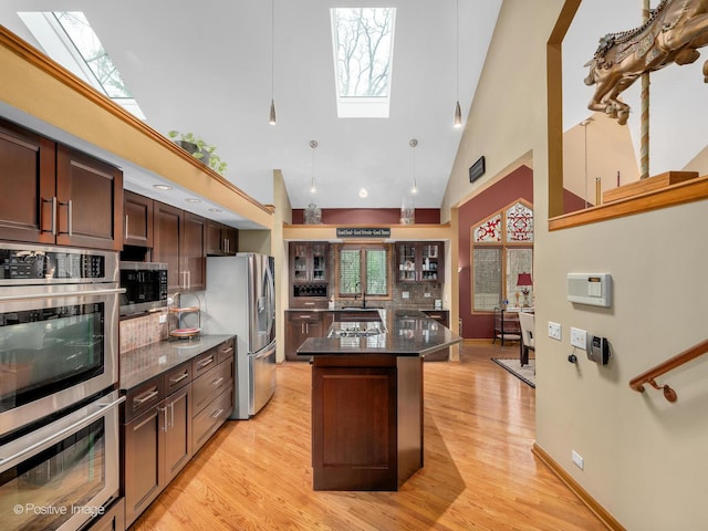 kitchen featuring a kitchen island, high vaulted ceiling, a skylight, light hardwood / wood-style floors, and stainless steel appliances