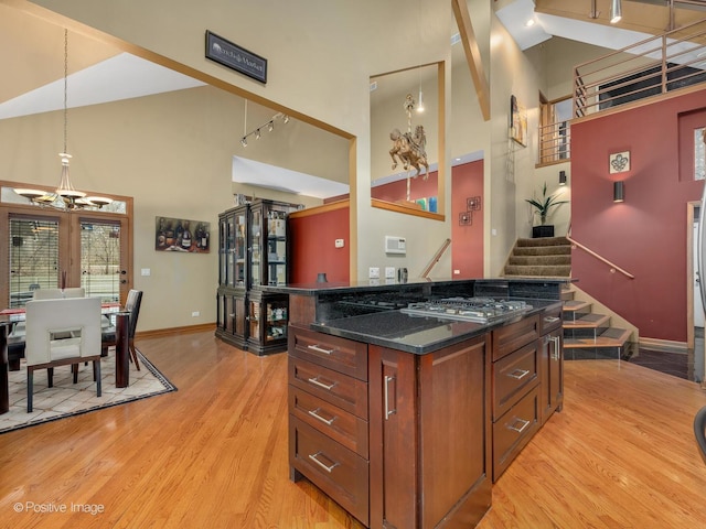 kitchen with a high ceiling, pendant lighting, dark stone countertops, and light hardwood / wood-style flooring