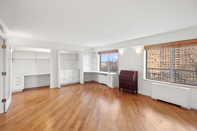 unfurnished bedroom featuring radiator, built in desk, and light wood-type flooring