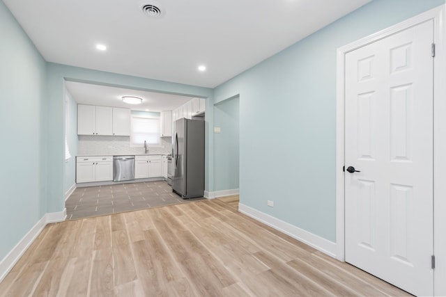 kitchen with white cabinetry, stainless steel appliances, decorative backsplash, sink, and light hardwood / wood-style flooring