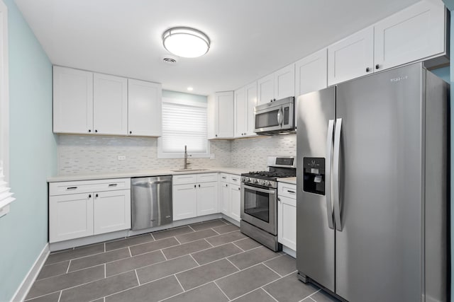 kitchen with appliances with stainless steel finishes, tasteful backsplash, dark tile patterned flooring, white cabinets, and sink