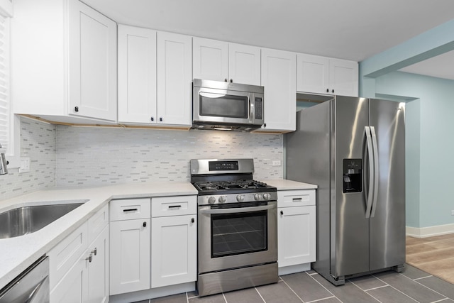 kitchen featuring appliances with stainless steel finishes, tile patterned flooring, white cabinetry, decorative backsplash, and sink