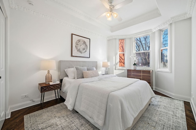 bedroom with dark wood-type flooring, ceiling fan, ornamental molding, and a raised ceiling