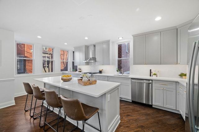 kitchen featuring sink, dark hardwood / wood-style floors, a kitchen island, stainless steel appliances, and wall chimney range hood