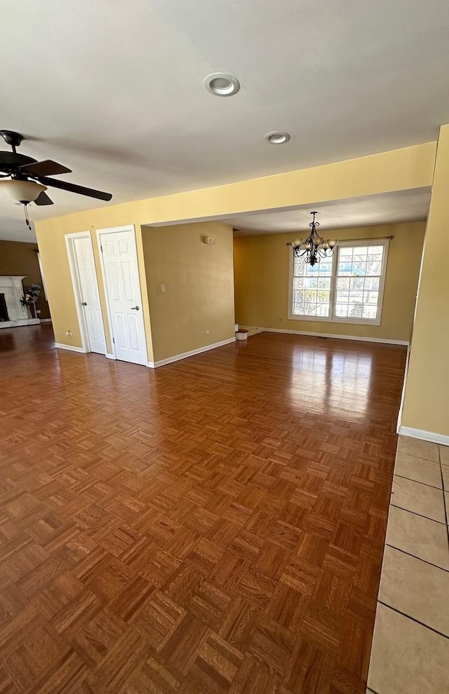 empty room with ceiling fan with notable chandelier and dark parquet floors