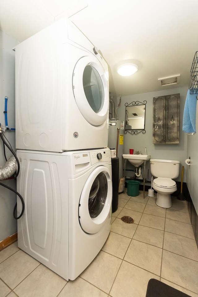 laundry room featuring sink, stacked washer and dryer, light tile patterned floors, and water heater