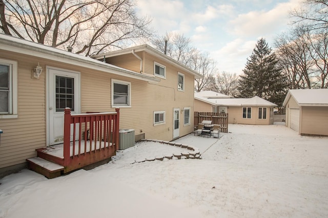 snow covered rear of property with central AC unit, a garage, and an outdoor structure