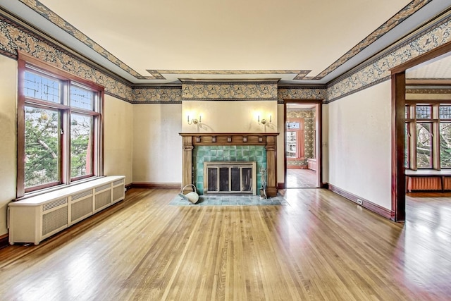 unfurnished living room featuring hardwood / wood-style floors, radiator heating unit, ornamental molding, and a fireplace