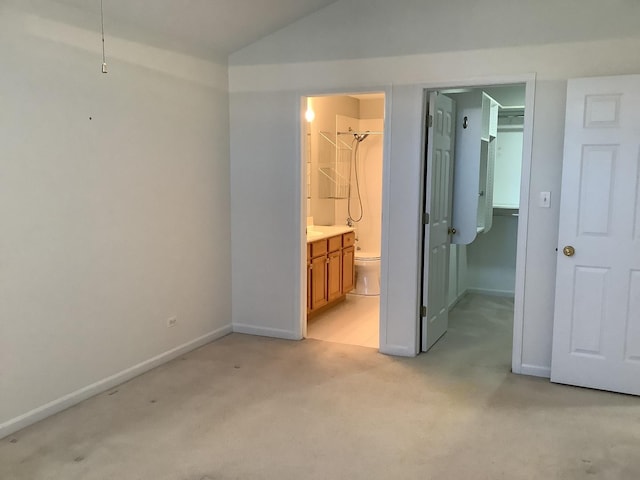 unfurnished bedroom with light carpet, ensuite bath, a walk in closet, a closet, and lofted ceiling