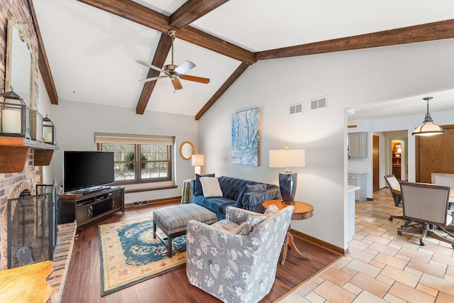 living room featuring a brick fireplace, light hardwood / wood-style floors, ceiling fan, and vaulted ceiling with beams