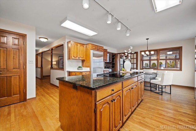 kitchen featuring black electric stovetop, built in fridge, a notable chandelier, a center island, and light wood finished floors